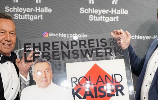 Roland Kaiser und René Otterbein halten den Ehrenpreis in Form einer Plexiglasplatte und lachen in die Kamera.