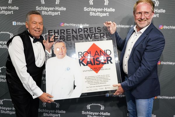 Roland Kaiser und René Otterbein halten den Ehrenpreis in Form einer Plexiglasplatte und lachen in die Kamera.